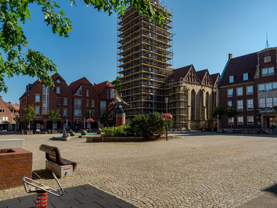 Vollständig eingerüsteter Kirchturm an einem Marktplatz mit Backsteinhäusern