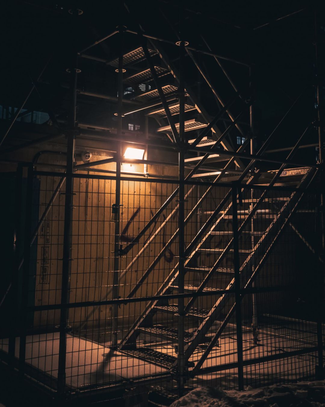 Treppenläufe und Podeste eines Gerüstturms bei Nacht, von einem Scheinwerfer angeleuchtet